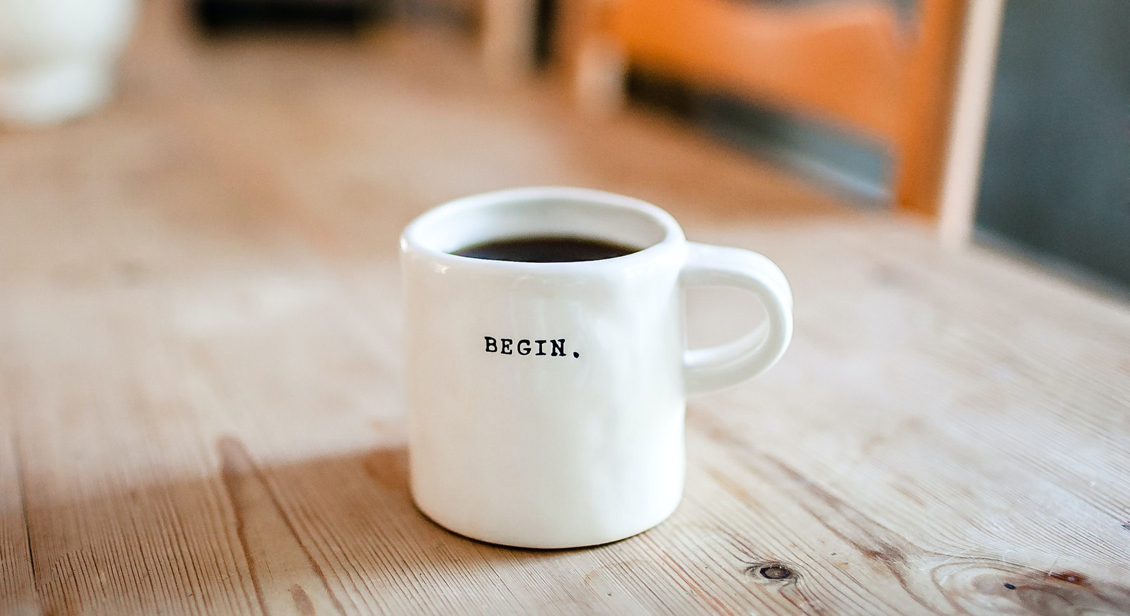 A white mug of coffee stamped with the word BEGIN on a café table